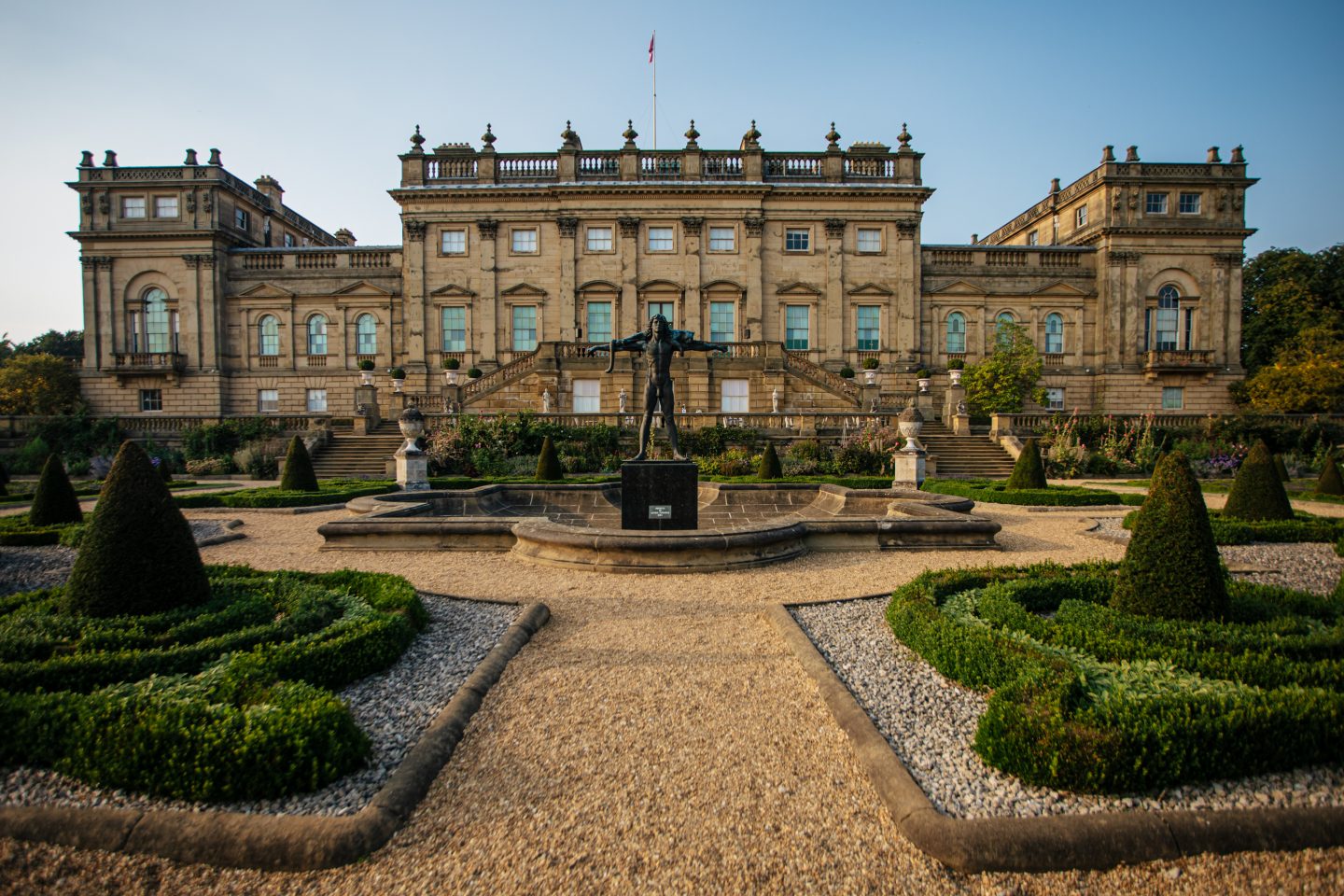 Bronze statue of Orpheus stands proudly in the middle of an ornate pool of water on the Victorian Terrace. A grand historic Georgian House bathed in the soft glow of the evening light stands in the background.