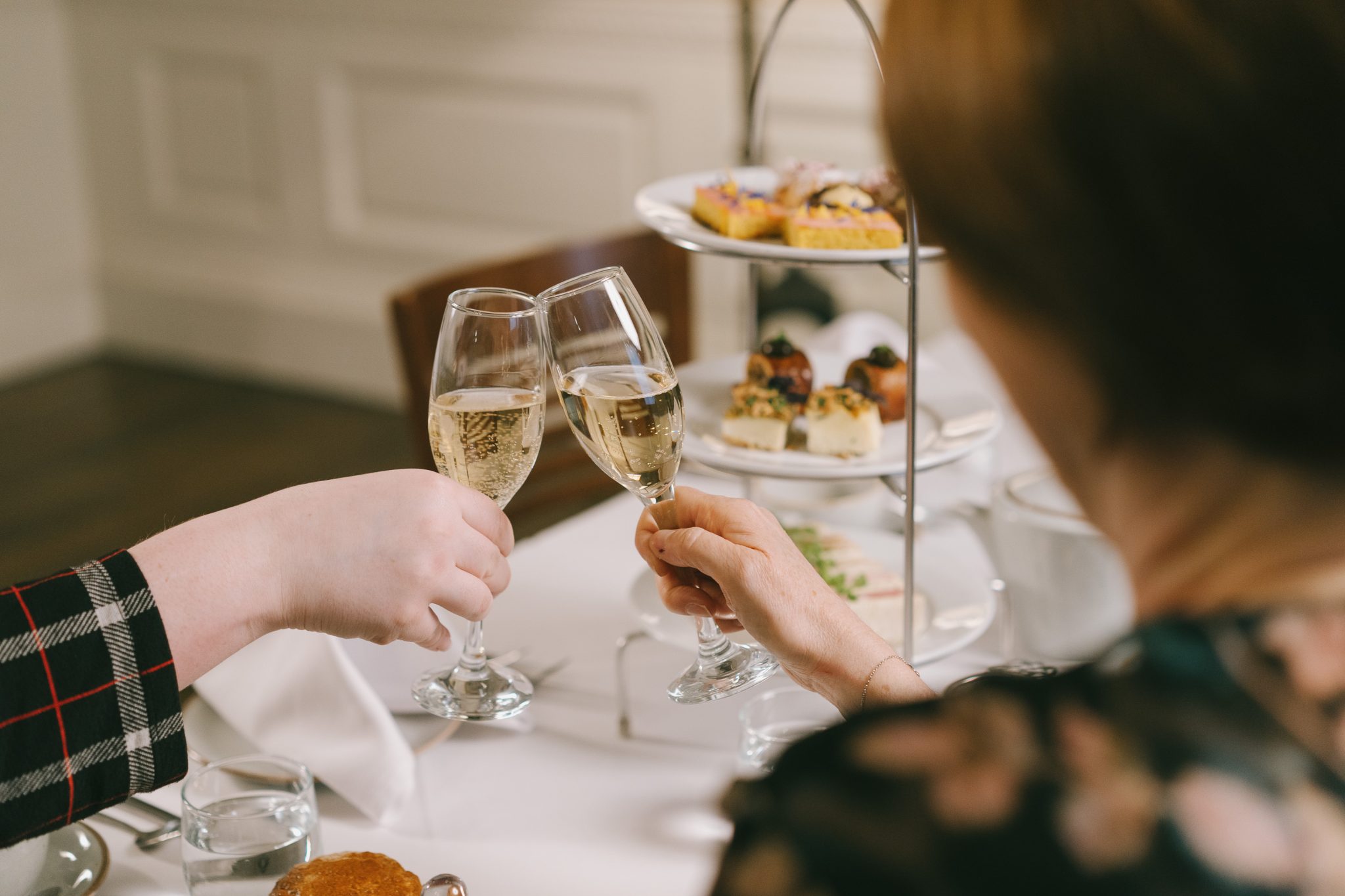 Two people hold a flute glass of sparkling wine each and cheers before tucking into Afternoon Tea.