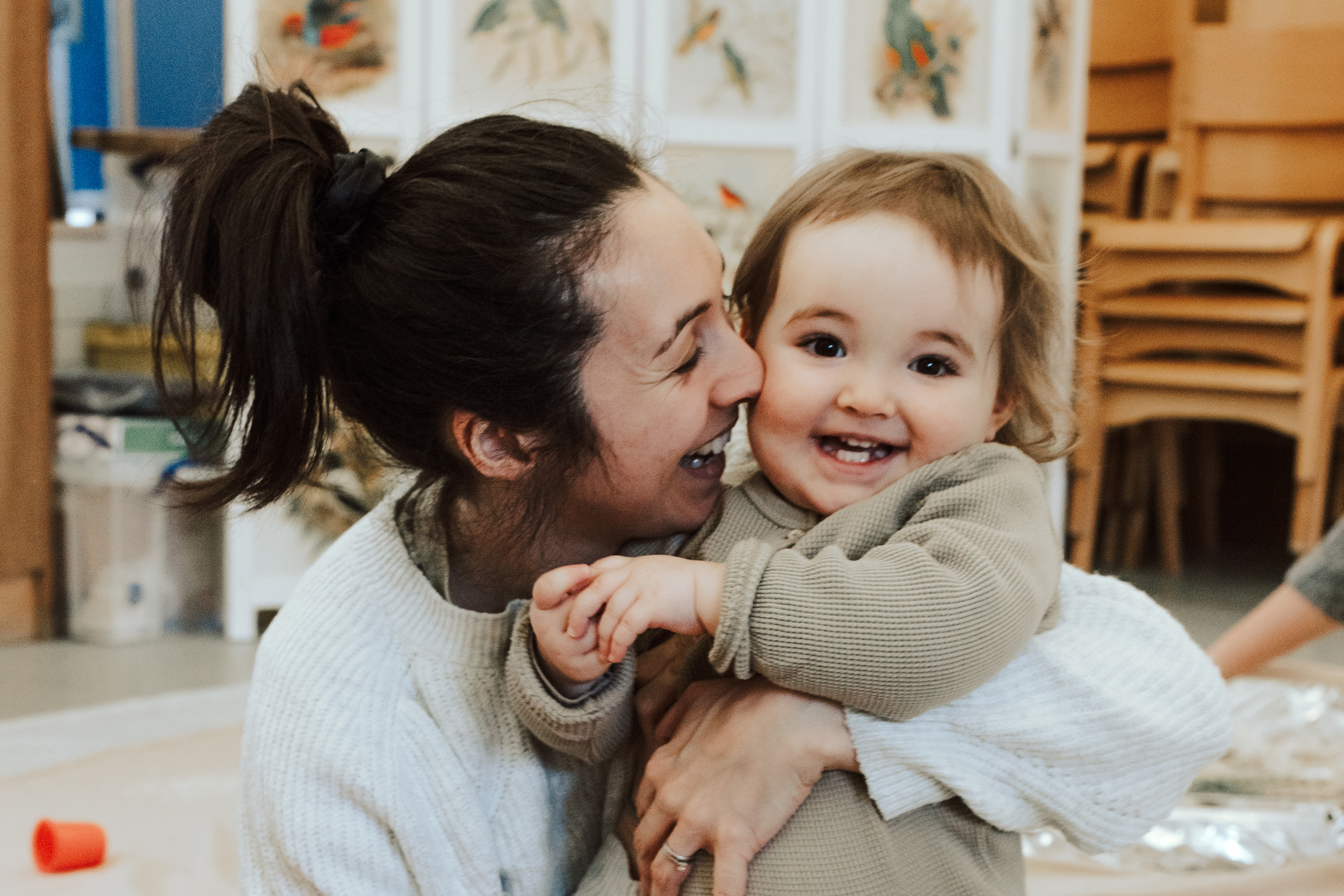 A close-up of a woman and child sharing a heartwarming embrace. The child looks at the camera with a big smile, while the woman leans in, creating a sense of warmth, fun and love.