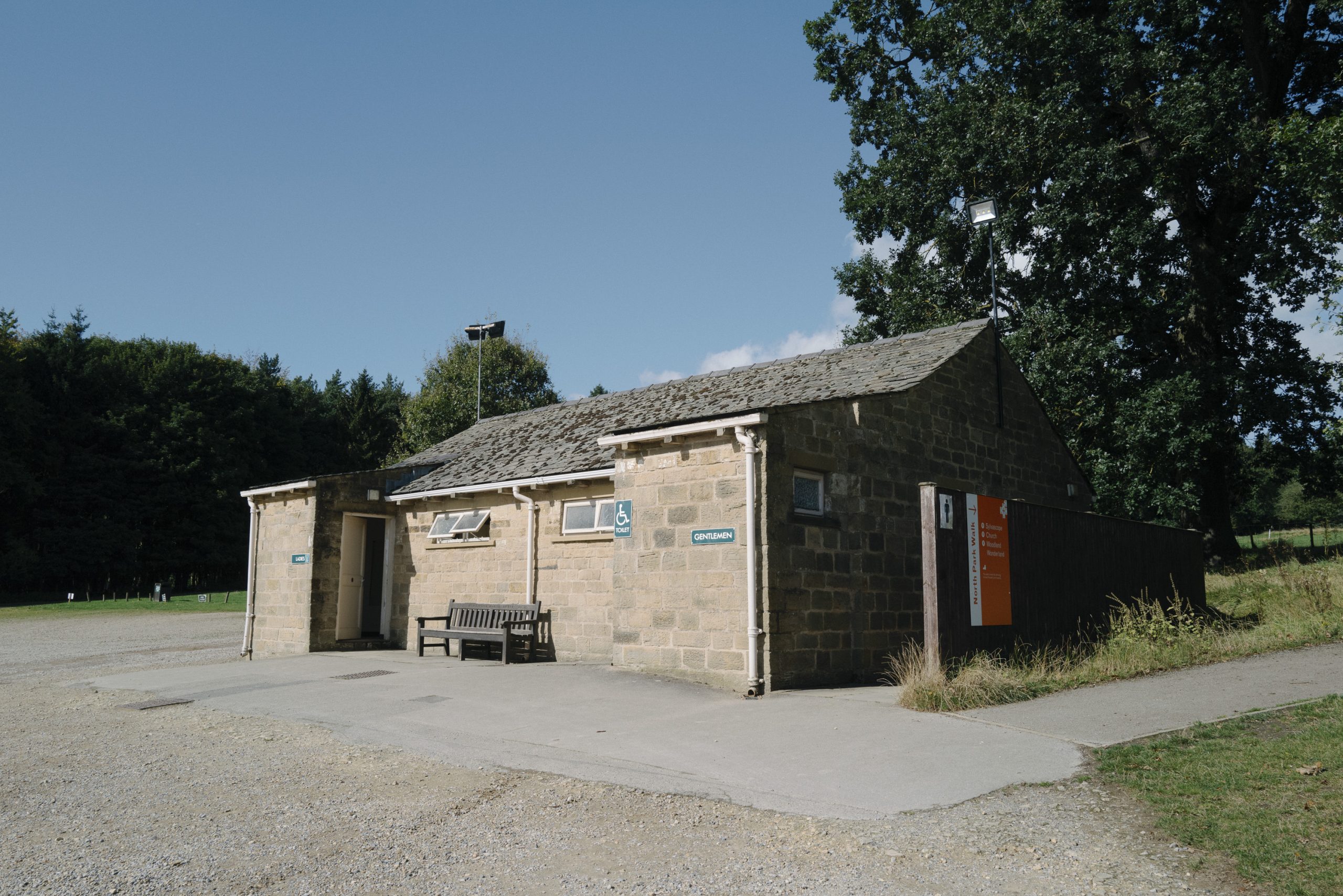 Small stone building stands at the top of the car park with toilets on either side and a bench outside.