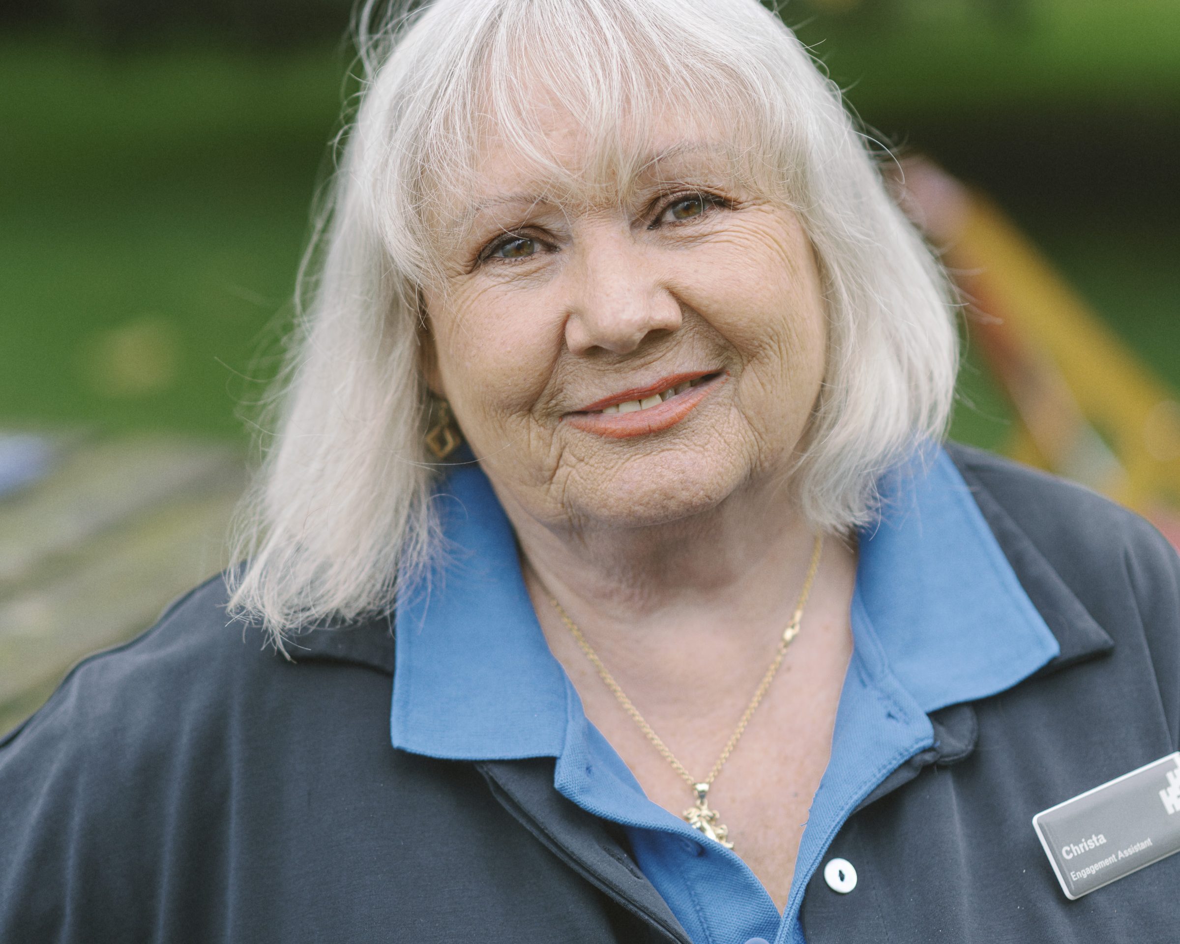 Woman with shoulder length blonde hair, in a blue polo shirt with a black jacket. On her jacket she wears her name badge on the right hand side.