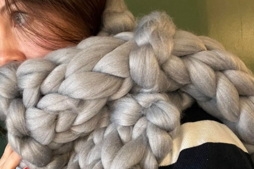 A woman wrapped up in a chunky scarf made of a silvery-grey wool. Only her eyes are visable and she looks cosy and warm.