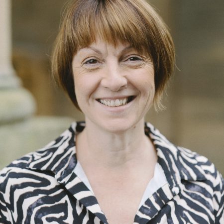 A smiling person with chin-length brown hair, wearing an animal print shirt dress