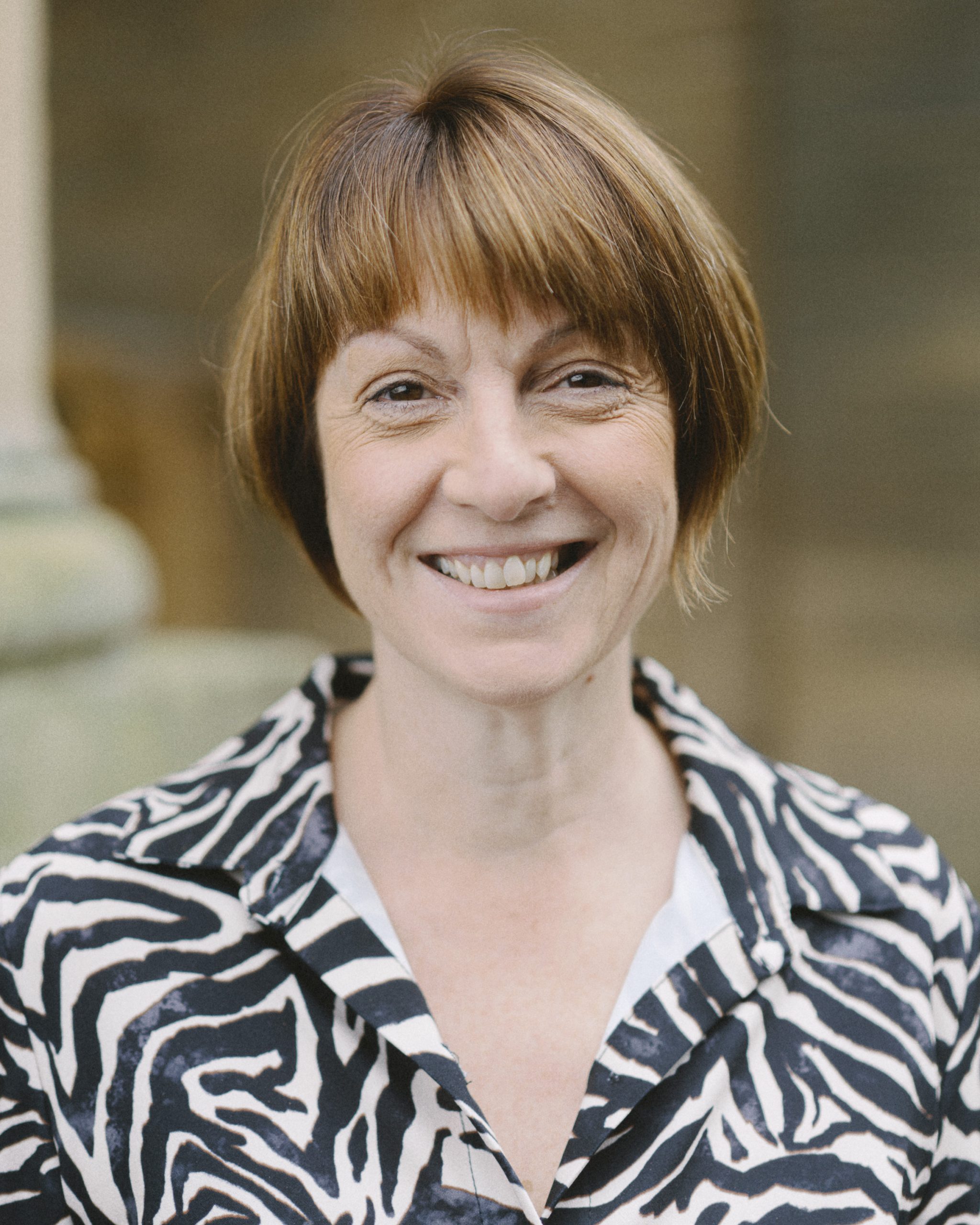 A smiling person with chin-length brown hair, wearing an animal print shirt dress