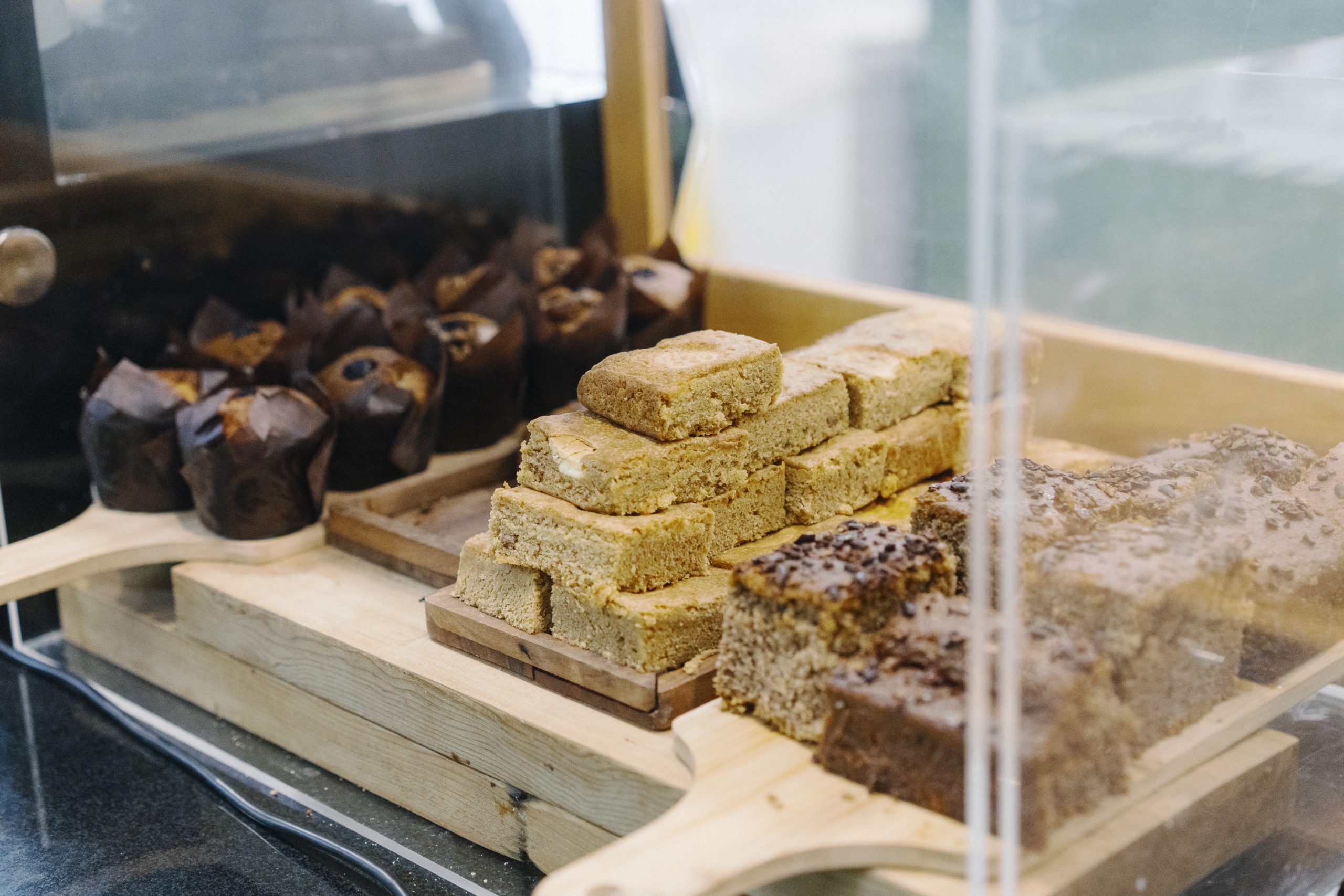 Light wooden chopping boards placed on the Courtyard Cafe counter tops piled high with freshly baked Blueberry Muffins, Jammie Dodger Blondies and thick slices of seed topped vegan Banana Bread