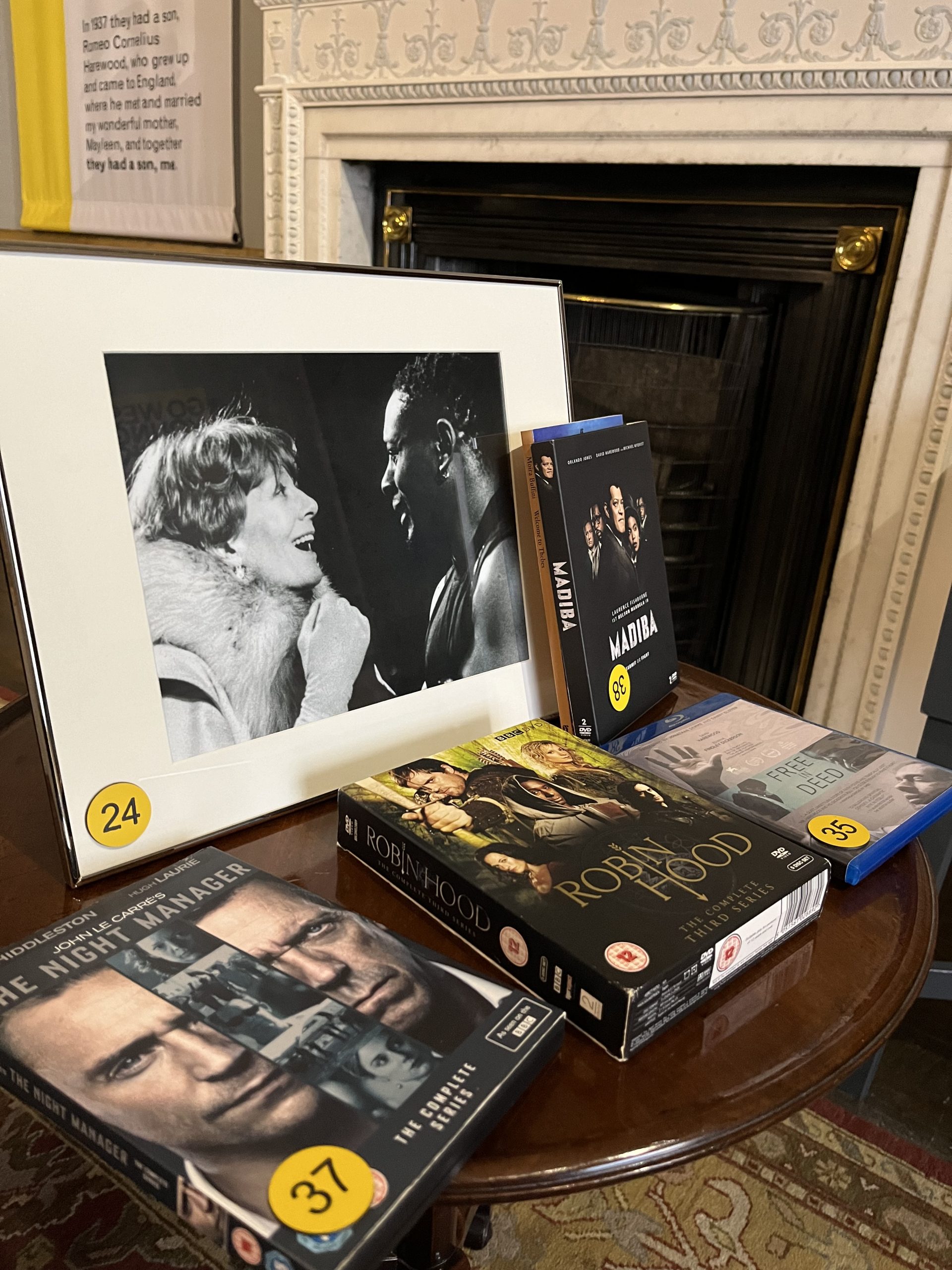 Framed black and white photo of David Harewood and an actress surrounded by DVDs titled: The Night Manager, Robin Hood, Free in Deed and Madiba