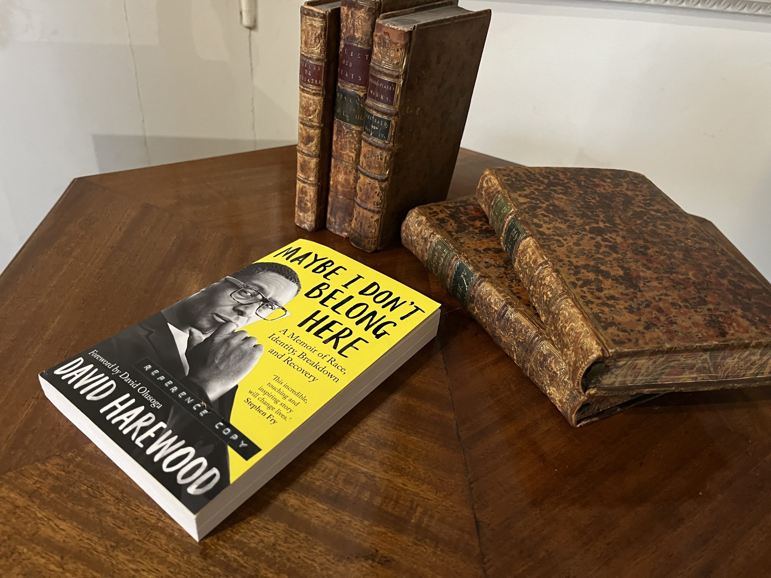 Upon a wooden table stands David Harewood's memoir "Maybe I don't belong here" alongside vintage and rare books from Harewood's collection