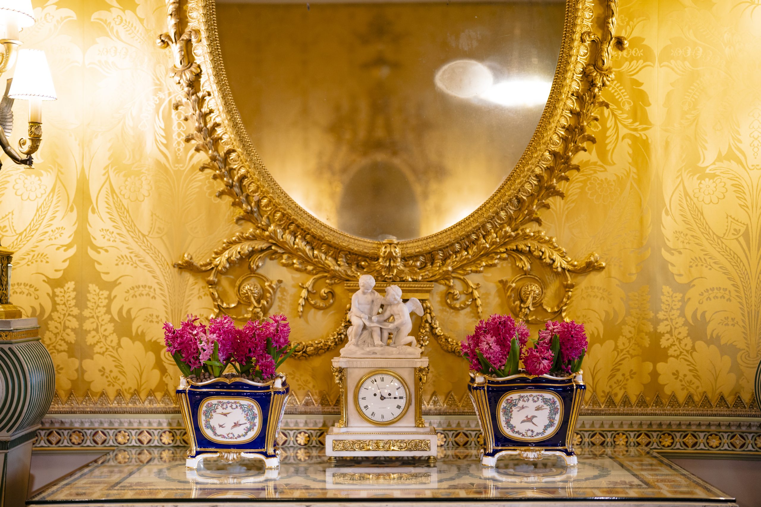 A marble clock and cherub statue are flanked by vibrant pink hyacinth flowers planted into blue Sèvres porcelain.