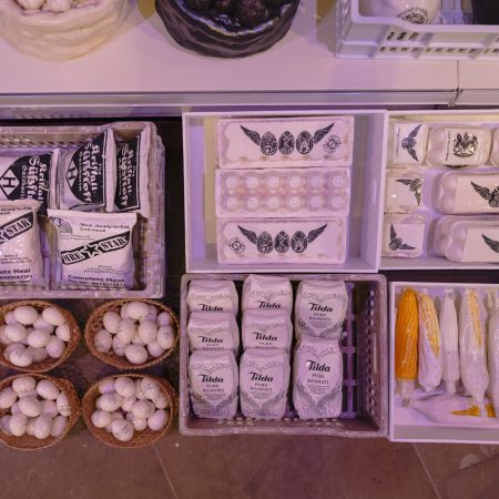 Close up detail of white porcelain market items, including eggs, Tilda pure basmati rice, corn on the cob and MRE (Meals Ready to Eat) bags.