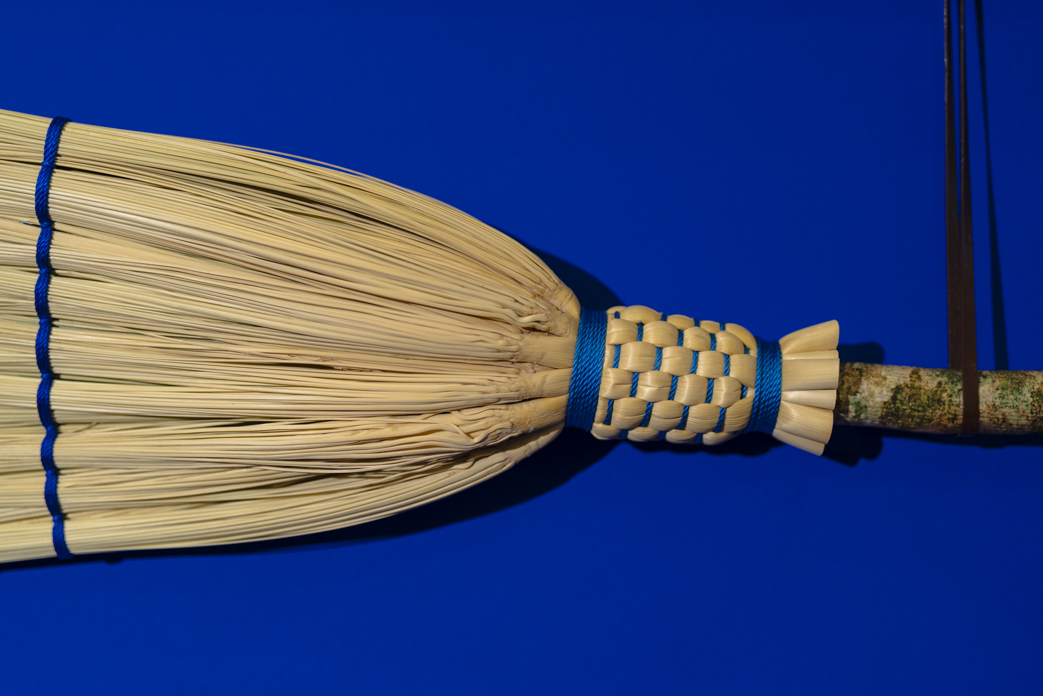 Detail of Rosa Harradine's double ended brook made from broomcorn, spalted hazel wood, nylon and leather. Broomcorn is a natural fibre, a type of sorghum. The wooden handle was harvested Rosa from my small patch of woodland in Carmarthenshire, Wales, sanded by hand and oiled with raw linseed oil.