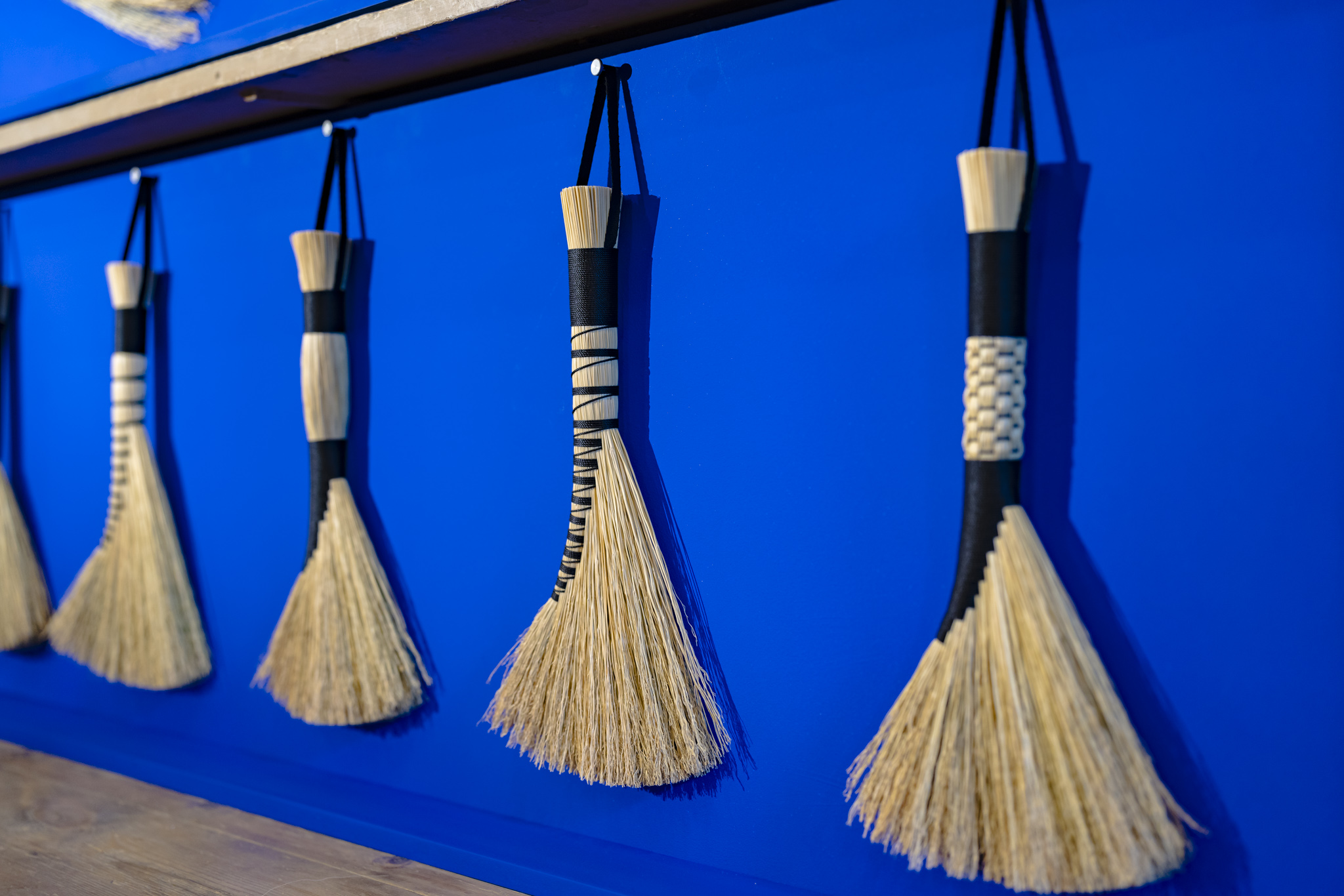 Detail shot of Rosa Harradine's hand crafted brushes made from broomcorn, hemp cord and cotton strap. Broomcorn is a natural fibre, a type of sorghum. It is stiff but has wispy ends, ideal for sweeping dirt and dust.