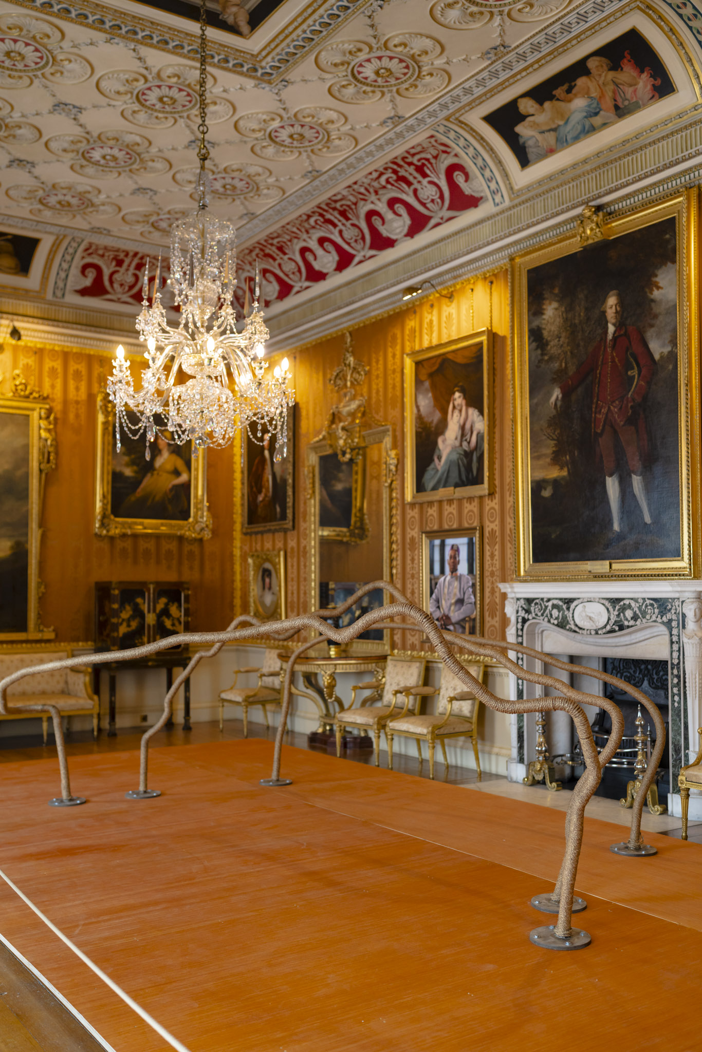 Wide view of the Cinnamon Drawing Room. Temitayo Ogunbiyi sculpture You Will Find Lagos in Jand living stands beneath a grand decorative ceiling where a crystal chandelier hangs.