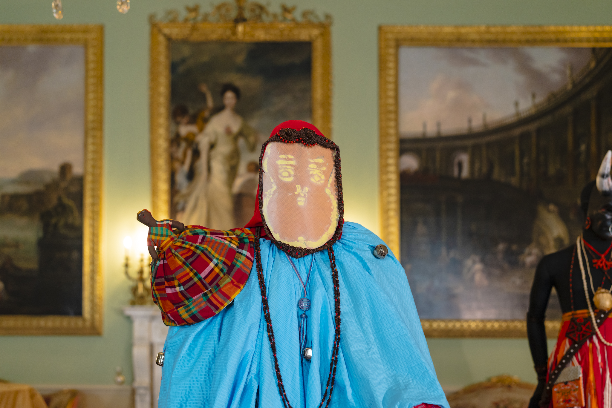 Mannequin stands in the middle of Harewood's Music Room wearing a bright blue Antigua and Barbuda Carnival costume, leather mask and red headdress adorned with tamarind seed jewellery.