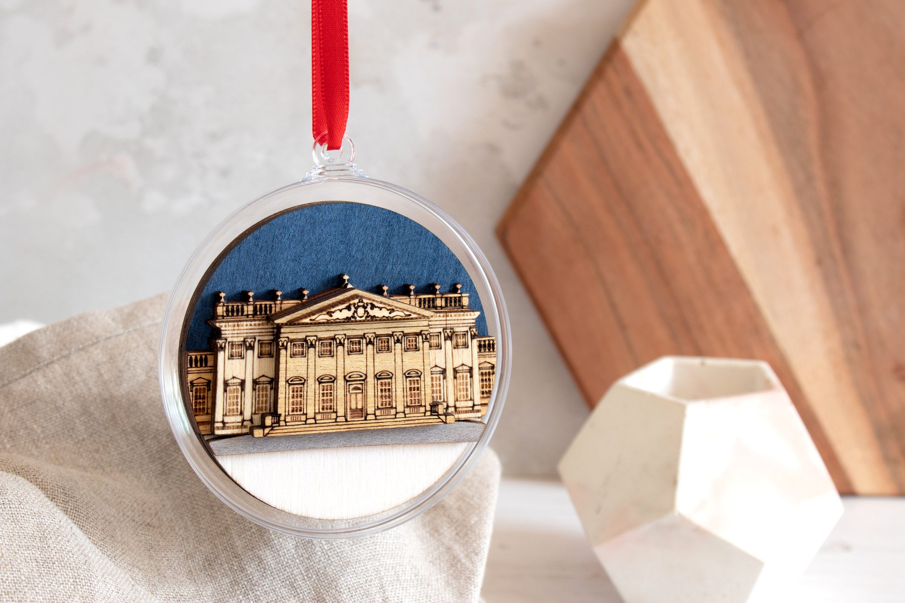 Harewood House carved out of wood inside a clear bauble with a dark blue sky, sealed with a red ribbon