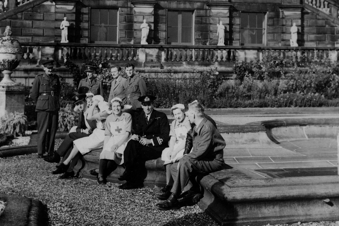 Black and white photograph from WWII when Harewood was a convalescent hospital. Military patients sit outside on the Terrace enjoying the sunshine with Nurses and Doctors.