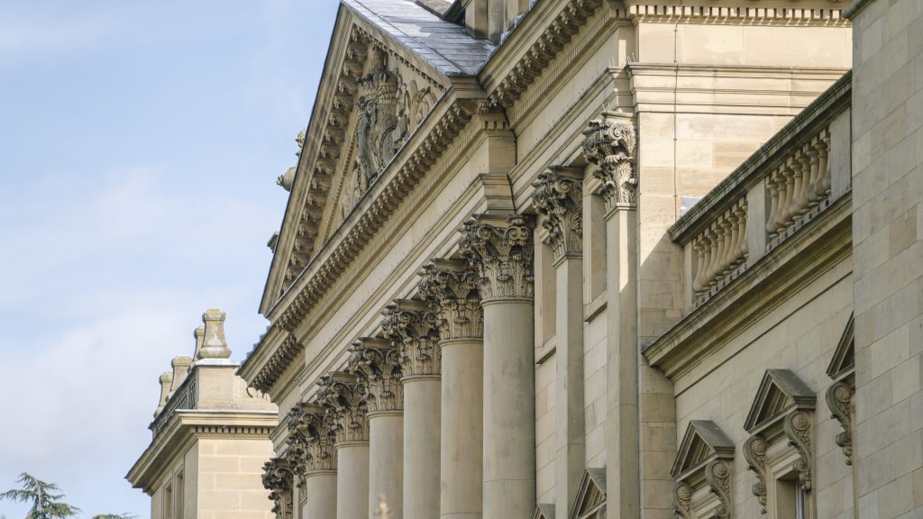 Side view of Harewood House showcasing the detailed architecture designed by York architect John Carr in the Palladian style. A grand, symmetrical façade with a central portico supported by six classical columns, large sash windows, and intricate stone detailing.