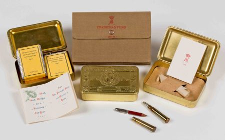 A selection of embossed brass Christmas gift boxes showing their contents, including tobacco packets, bullet case pencils and christmas cards from Princess Mary.