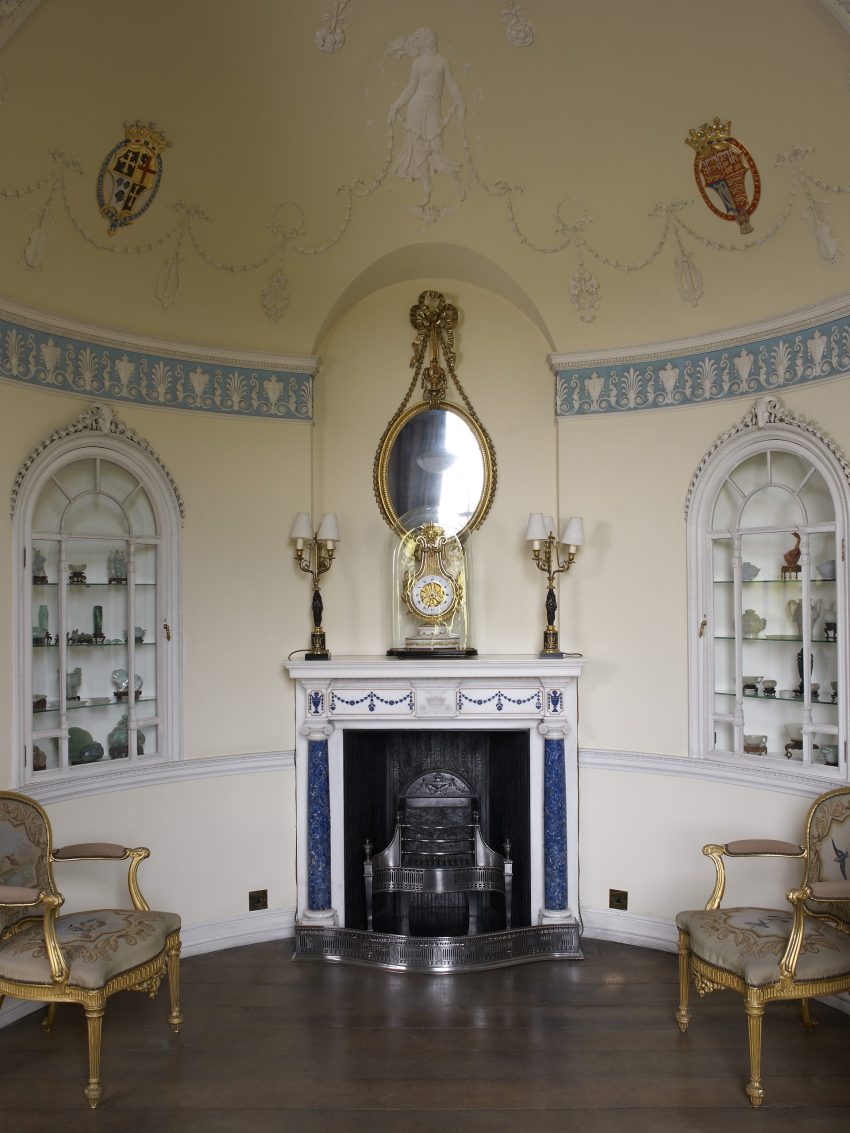 An alcove with a fireplace in the centre and two arched display cabinets to the left and right. The mantlepiece is decorated with lapiz lazuli columns and detailing, and a large lyre-shaped clock sits on top.