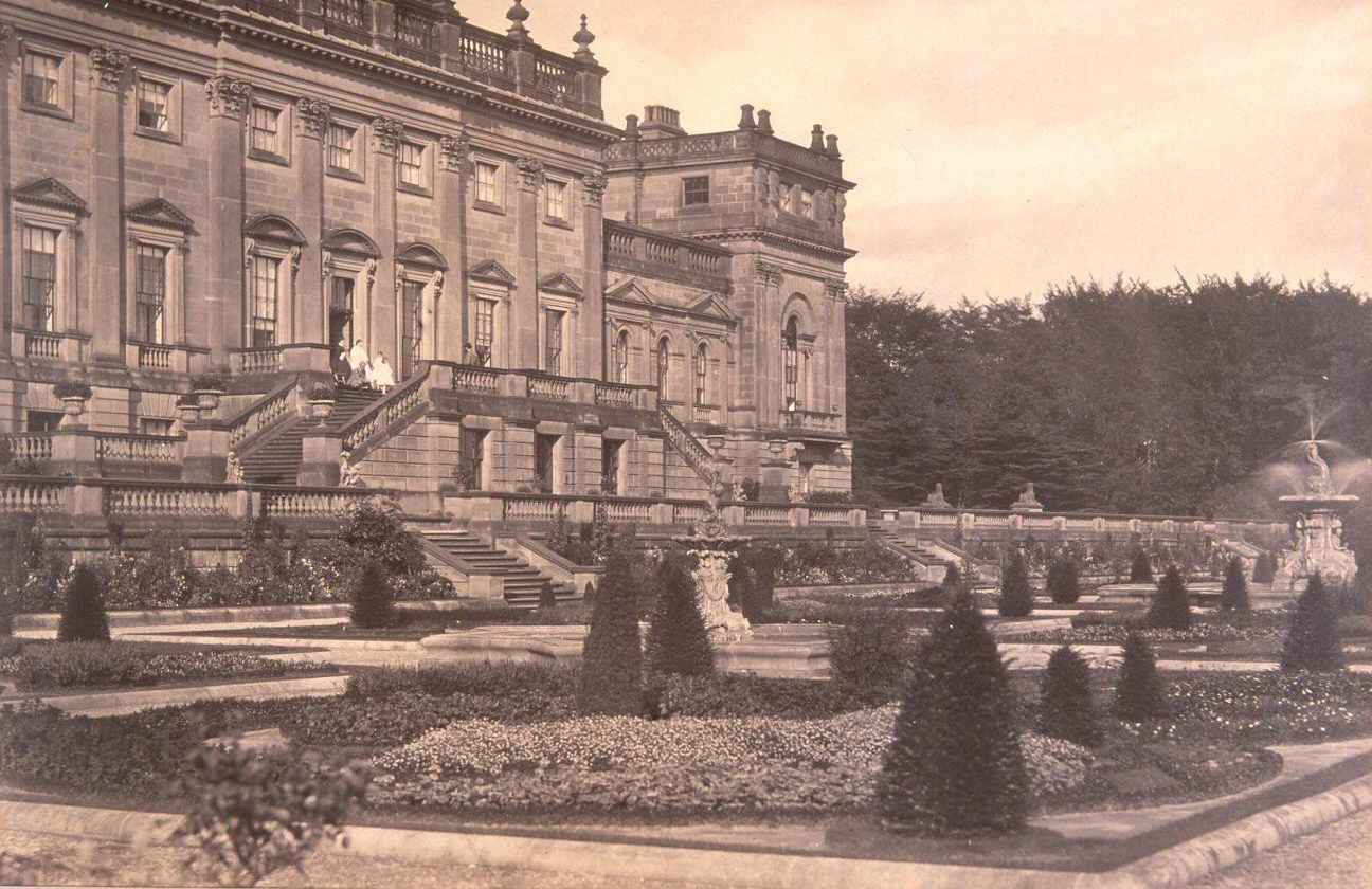 Sepia photograph of the Victorian Terrace captured in the mid 1800s. The parterre features an intricate design of shrubbery, ornamental plants and rose borders. In the background, the Lascelles Family stands on the top level of the Terrace.