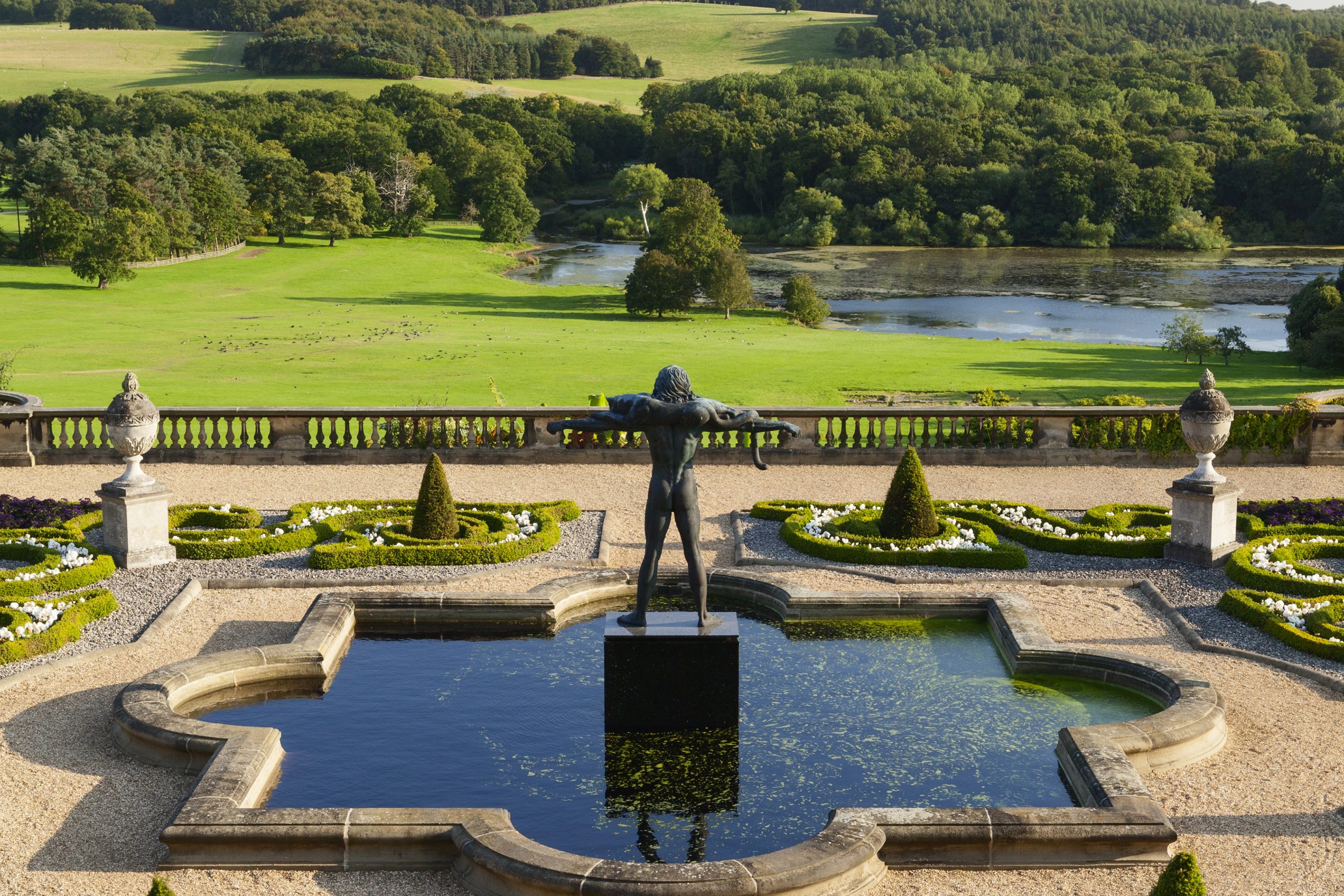 Clear blue skies sit above the rolling Capability Brown landscape with trees dotted across the horizon. Orpheus stands proudly in the middle of an ornate pool of water on the Victorian Terrace.