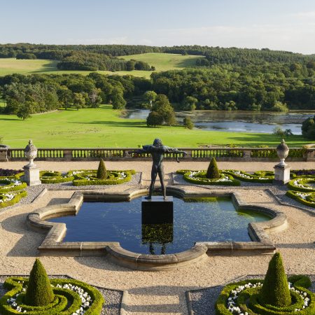 Clear blue skies sit above the rolling Capability Brown landscape with trees dotted across the horizon. Orpheus stands proudly in the middle of an ornate pool of water on the Victorian Terrace.