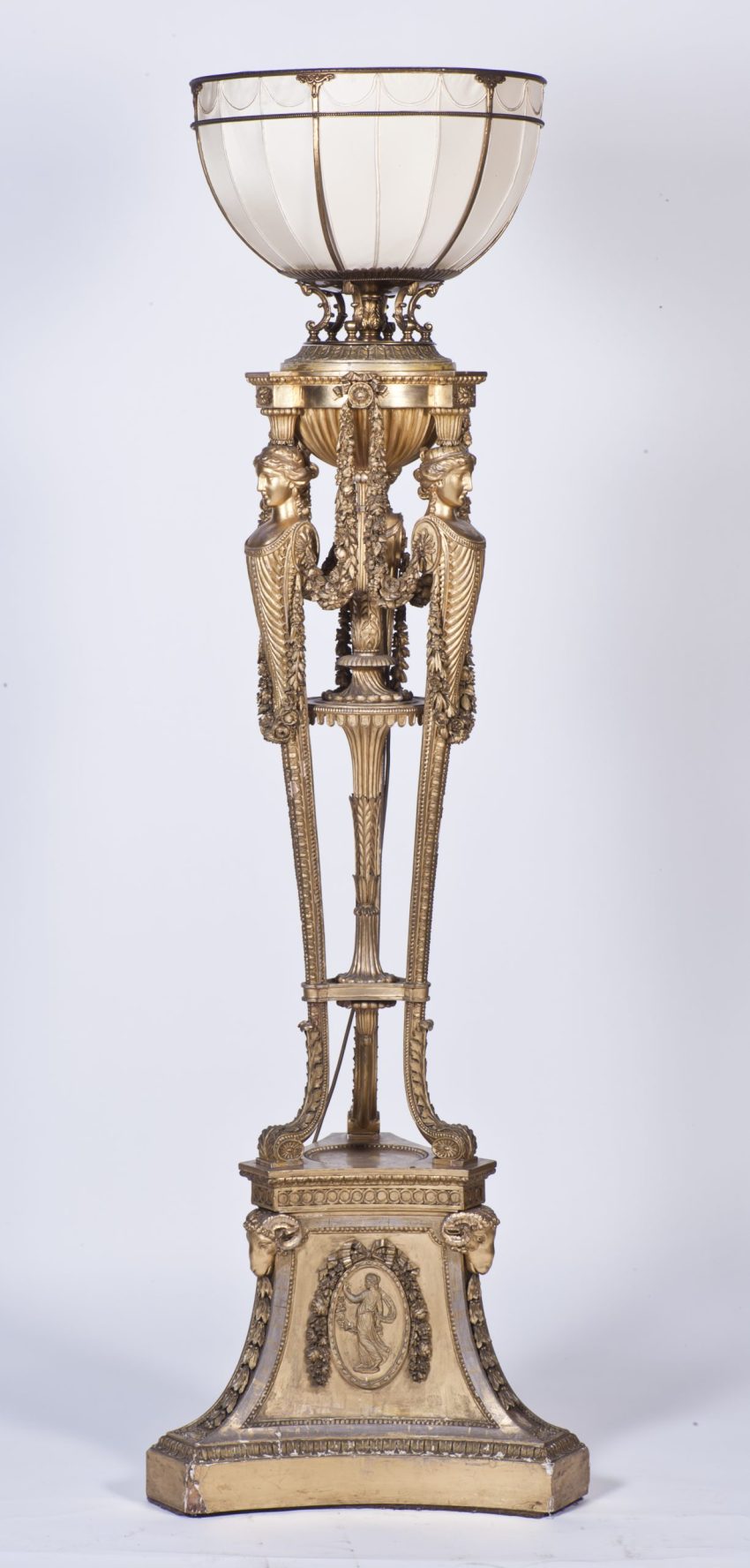 A gilded and elaborately carved tripod stand with a bowl-shaped shade at the top.