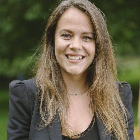 A smiling lady with long brown hair, wearing a black blazer