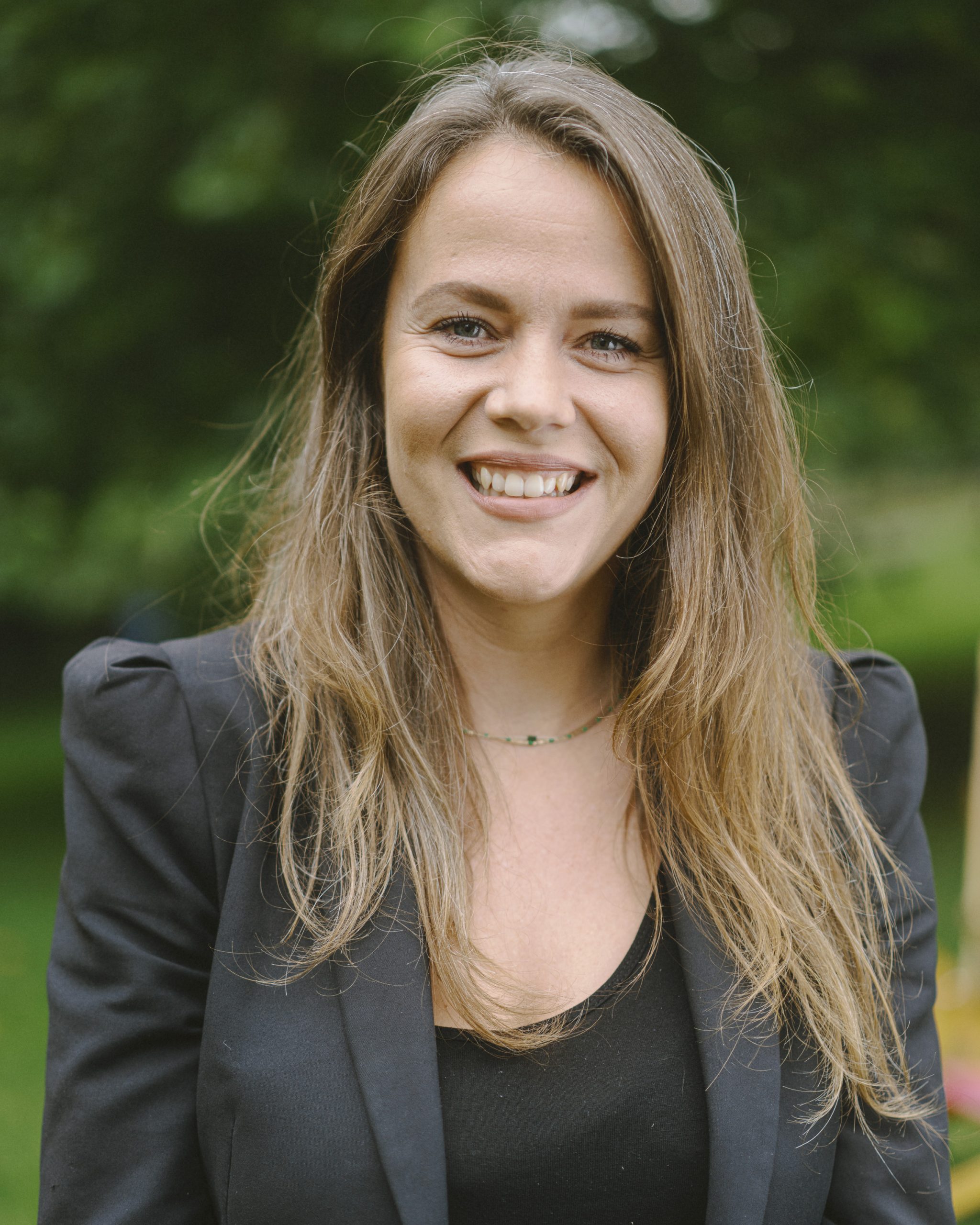 A smiling lady with long brown hair, wearing a black blazer