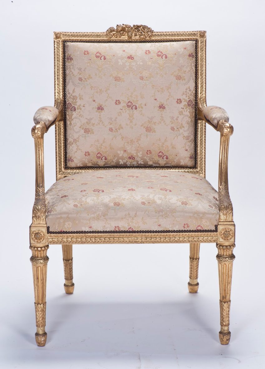 A gilded carved arm chair with a square seat and back, upholstered in white damask.