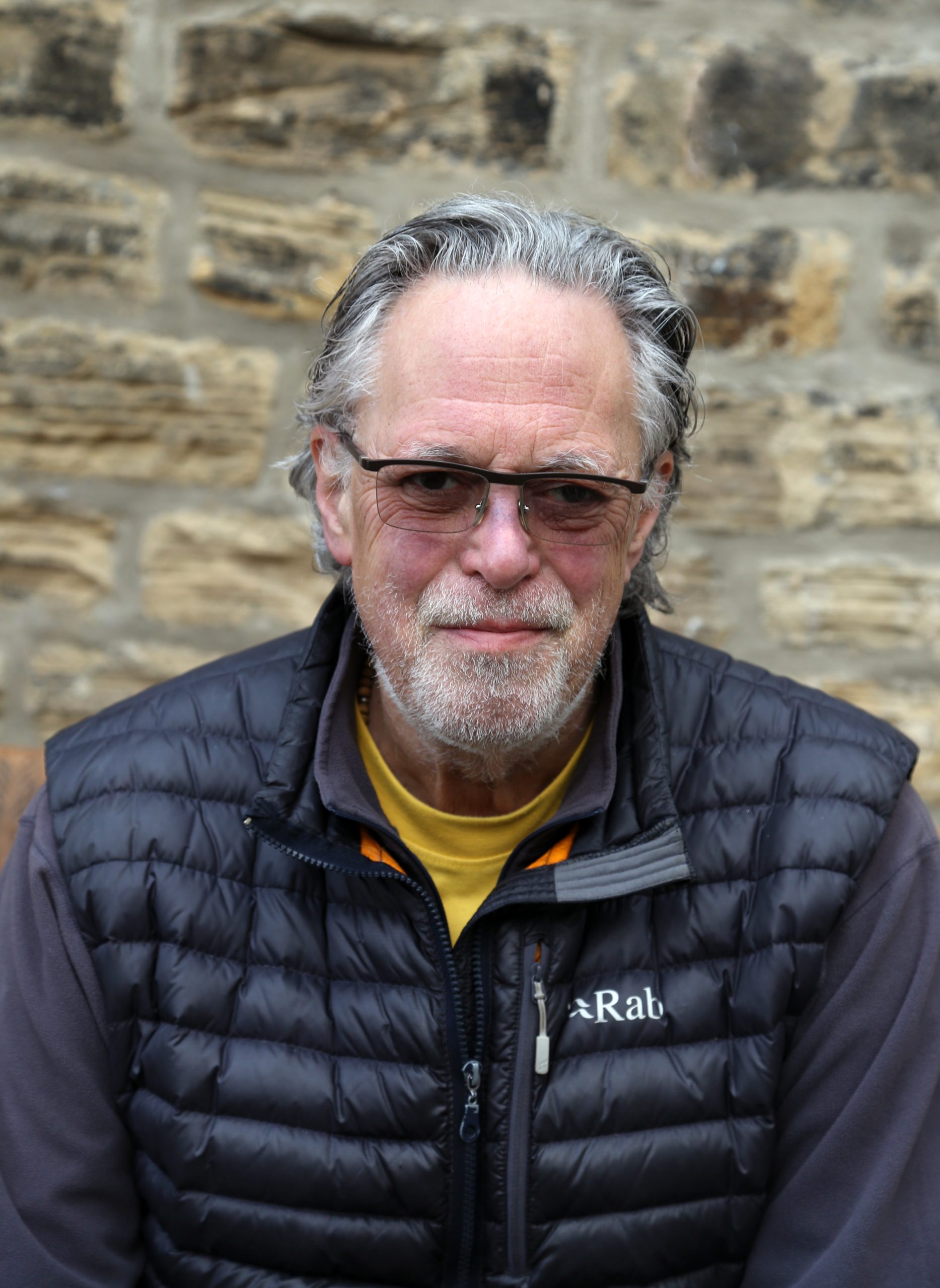 David Lascelles, Earl of Harewood. David has grey hair and a beard, and is wearing a padded black jacket and tinted sunglasses.