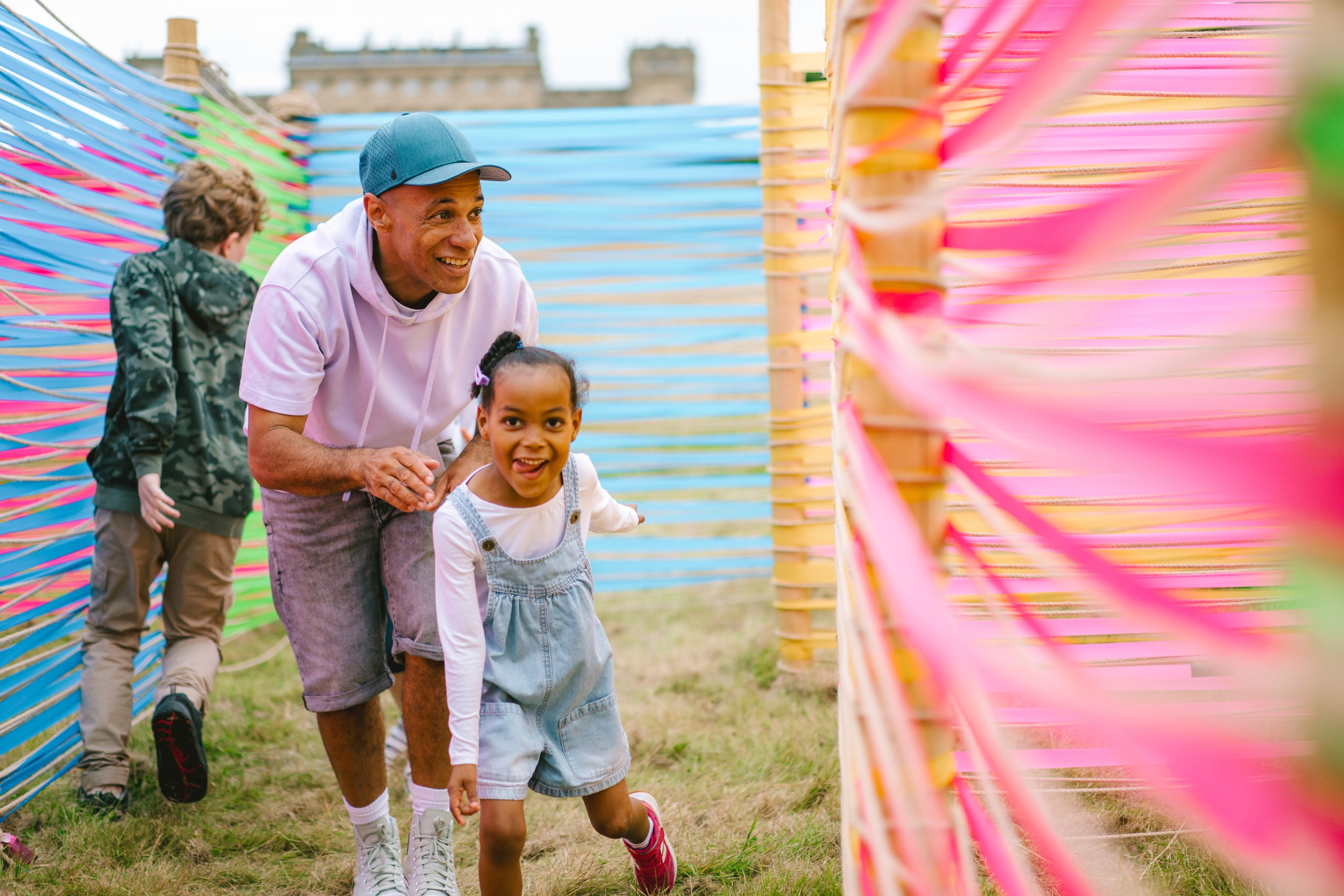 A father and daughter are in motion against a brightly coloured background. Harewood House is just visible in the background.