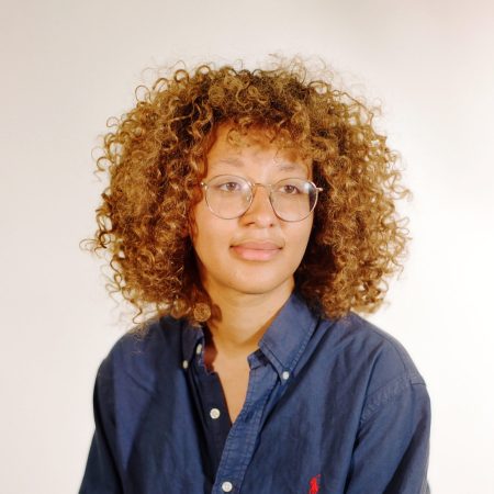 Mireille Harper, a 29-year-old mixed race woman with light brown curly hair, wearing a blue shirt.