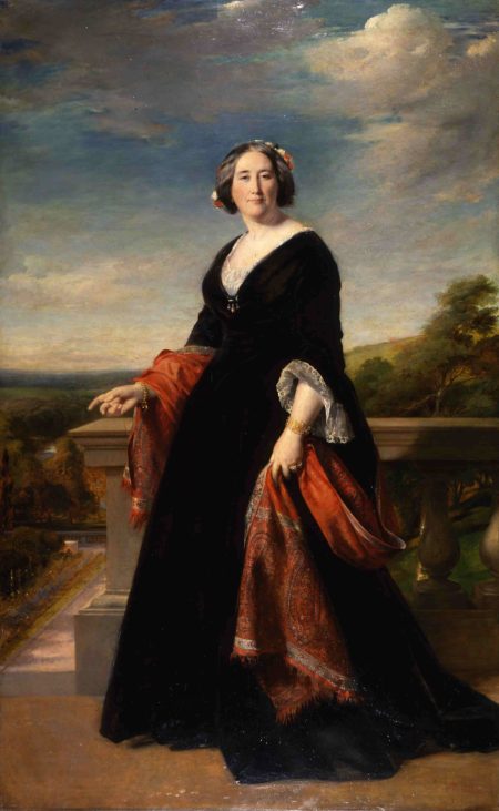 A full length oil portrait of a white, middle-aged woman. She wears a large black dress and a paisley shawl is draped loosely behind her back. Though she stares directly at the viewer, she points to the a formal terrace garden behind her.